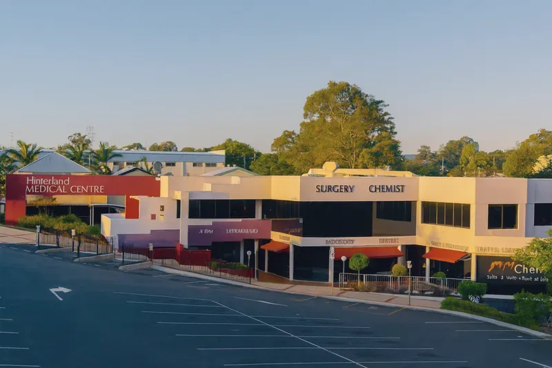 Hinterland Medical Centre on Price Street, Nerang, on a clear morning — a two-storey building with a red entrance block, surgery and chemist signage, and parking at the front.